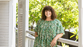 Woman in a green dress standing on a porch with trees in the background