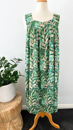 Green leaf-patterned dress on a mannequin against a white wall with a plant in the background.
