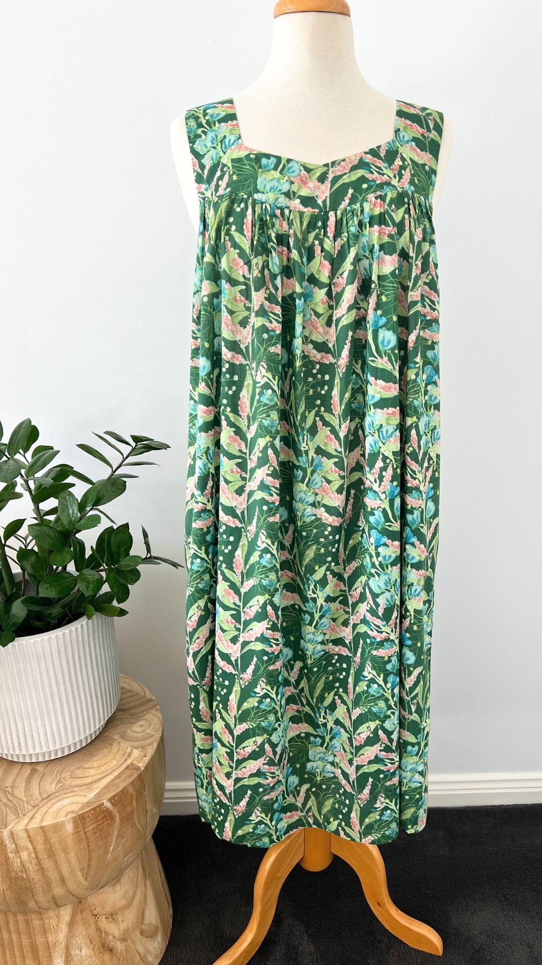 Green leaf-patterned dress on a mannequin against a white wall with a plant in the background.